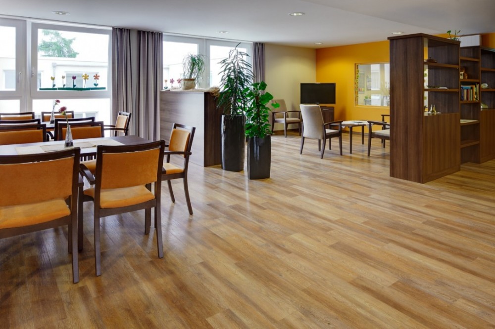 Gemütlicher Gemeinschaftsraum mit warmem Holzdesignboden und moderner Einrichtung Wohn- und Aufenthaltsbereich mit Designbelag in Holzoptik, Sitzgruppen und dekorativen Elementen